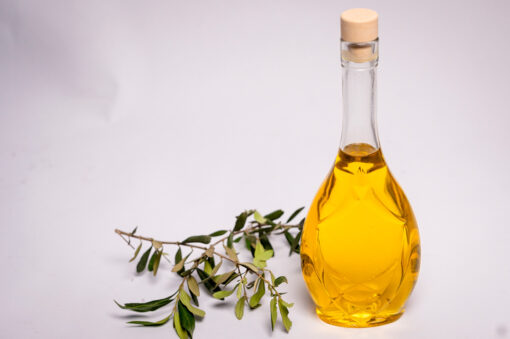 Bottiglia di vetro trasparente piena di Olio con un ramoscello di ulivo accanto.