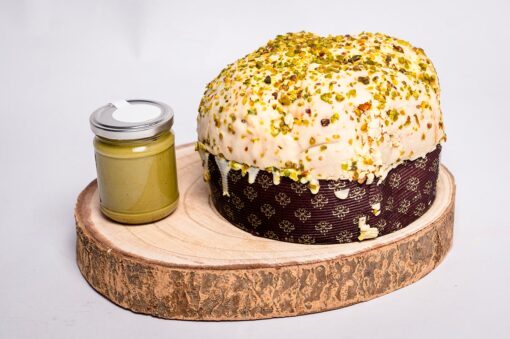 Un ceppo di legno usato come base per un panettone al pistacchio con accanto un barattolo di crema di pistacchio.